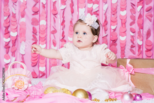 Baby girl with a Christmas balls in a festive pink interior