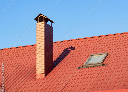 Brick chimney with skylight on the terracotta rooftop, closeup