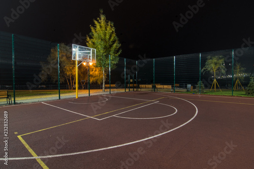 Illuminated basketball playground with red pavement, modern new basketball net and lens flares on background. 