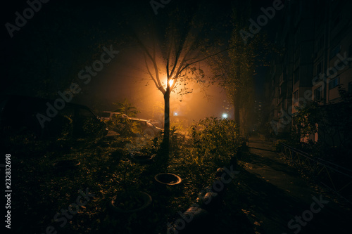 Fog night yard with bright light on background. Dark mood photo with green and orange colors