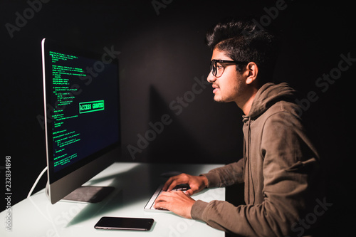 Indian man programmer working on desktop computer at white desk in office.