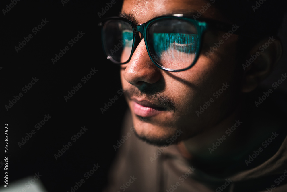 Hacker in glasses and a hood works at a computer in the dark, a reflection in glasses close-up. Hacker in glasses and a hood works at a computer in the dark, a reflection in glasses close-up.