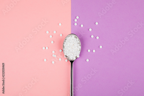 Foto Sugar-replacing tablets with a spoon on a pink and purple background
