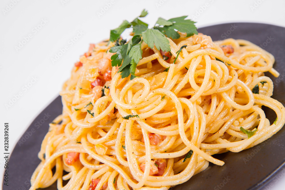 Spaghetti Carbonara with some parsley on a black plate on a white background