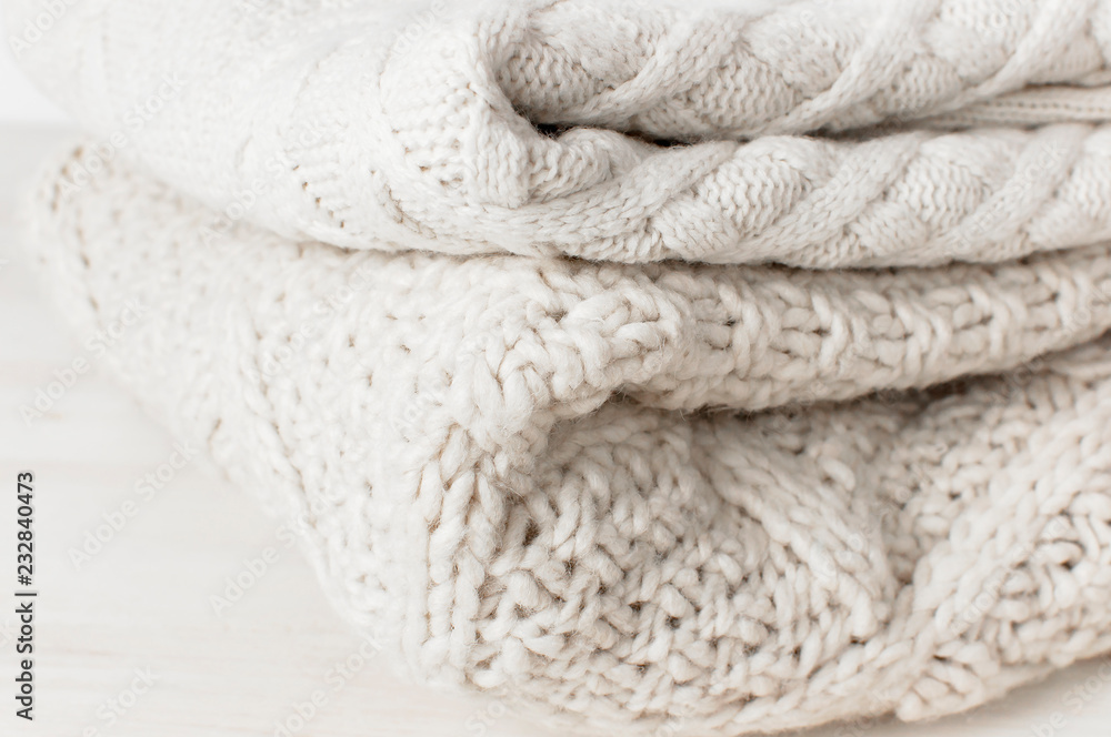 Two white knitted woolen sweaters pullover in a stack on wooden table on light background. Fashion Clothes Trendy Cozy Jumper. Autumn and winter clothes, space for text Two white knitted woolen sweaters pullover in a stack on wooden table on light background. Fashion Clothes Trendy Cozy Jumper. Autumn and winter clothes, space for text