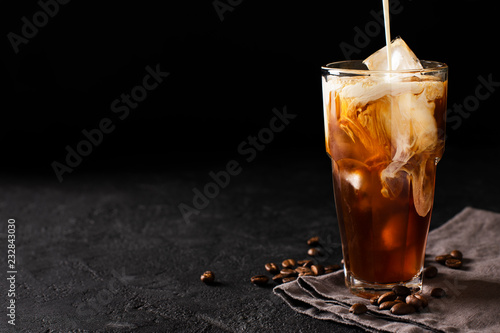 tall glass cold brew coffee with ice and milk on black or dark background