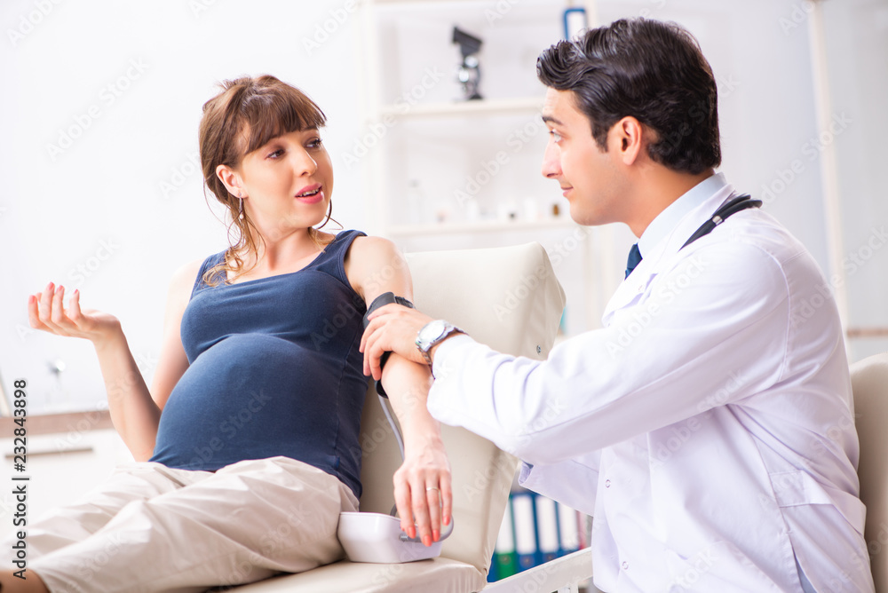 Fototapeta premium Young doctor checking pregnant woman's blood pressure
