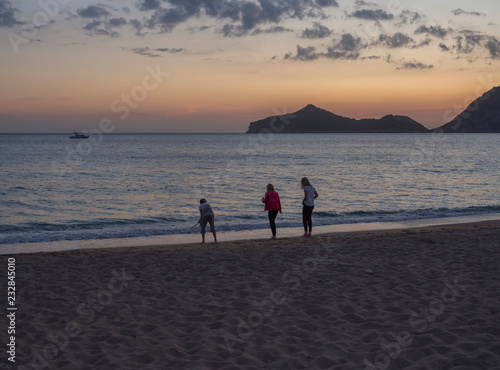 three childern playing on sea shore Agios Georgios Pagon beach at Corfu island  Greece at blue hour after pink orange sunset with view on porto timony bay