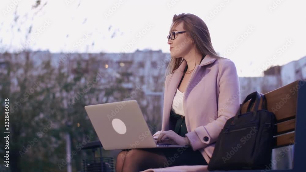 Pensive beautiful young woman working on laptop in city park in evening Pensive beautiful young woman working on laptop in city park in evening