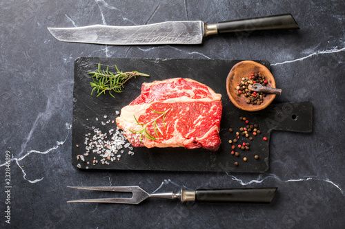 Raw Fresh Marbled Meat Beef Steak rosemary, spices slate on board. Black marble background. Top View Copy space for Text