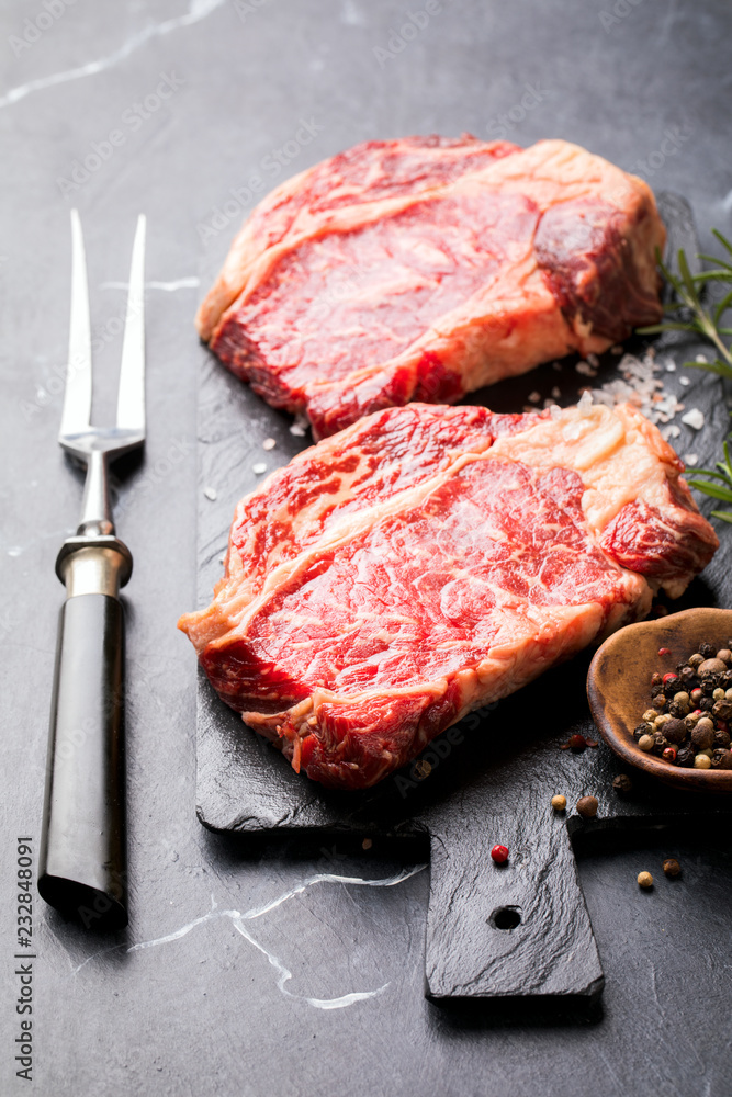 Raw Fresh Marbled Meat Beef Steak rosemary, spices slate on board. Black marble background. Copy space for Text Raw Fresh Marbled Meat Beef Steak rosemary, spices slate on board. Black marble background. Copy space for Text