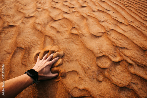 Man hand is touching sand in a desert at sunset