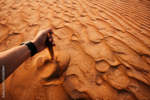 Male hand is pouring dropping sand in a desert at sunset