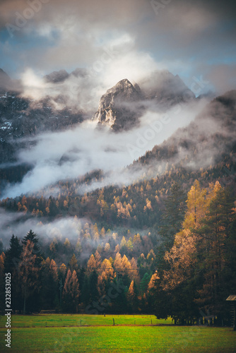 Fototapeta Naklejka Na Ścianę i Meble -  Autumn in mountains. Clouds and mist in orange forest under massive rock wall