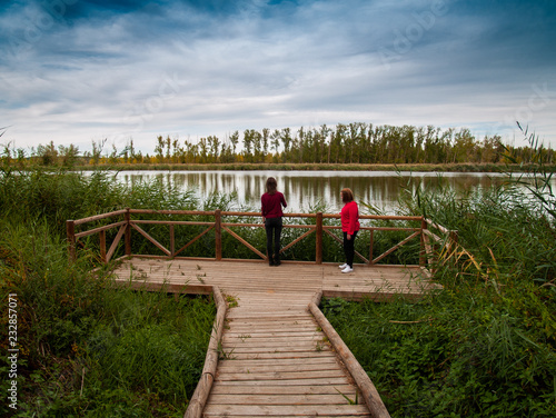 Two young women in a viewpoint with a wooden railing contemplating a river in autumn