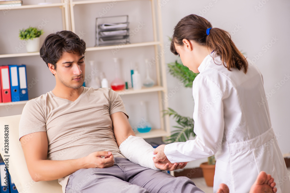 Young man with bandaged arm visiting female doctor traumatologis Young man with bandaged arm visiting female doctor traumatologis