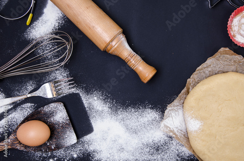 Obraz na plátně Powdering by flour rolled out dough for bakary stics  with wooden rolling pin over black basground
