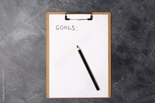 Blank paper with goals title and black pencil on grey table. Flat lay. Top view. New year concept. Free space. Copy space.
