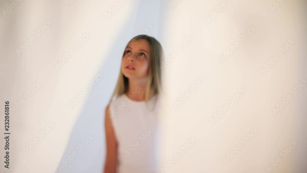Charming little girl stand in white dress with long hair talk sings looks around indoors cute young attractive blonde beautiful caucasian female pretty close up slow motion Charming little girl stand in white dress with long hair talk sings looks around indoors cute young attractive blonde beautiful caucasian female pretty close up slow motion