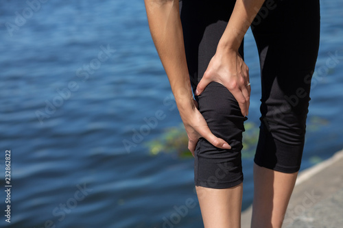Woman runner have muscle pain during running outdoors near the river. Empty space