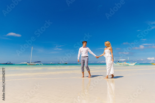 Happy Bride and Groom having fun on the tropical beach. Tropical sea and palm boats in the background. Wedding and honeymoon concept.