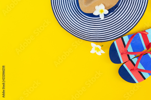 Summer flat lay scenery with hat, flip-flops sandals and flowers on bright yellow background with copy space