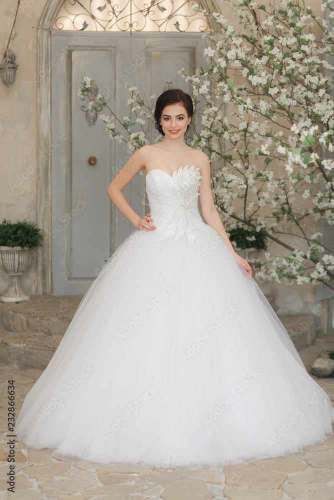 Young brunette bride in white luxury wedding dress. Old city background, full-lenght portrait. Smiling face