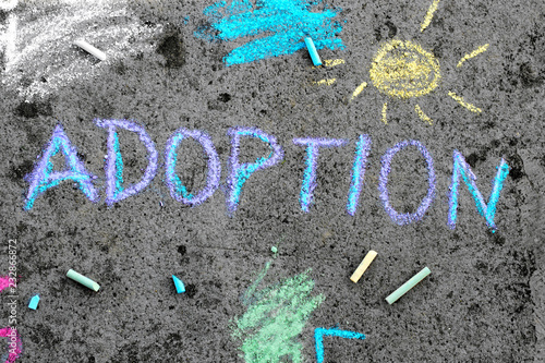 Colorful chalk drawing on asphalt: word ADOPTION