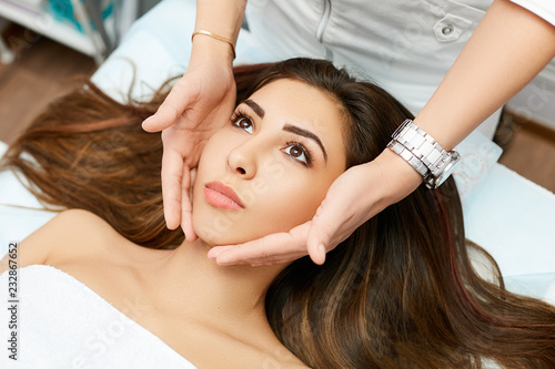 Brunette doctor cosmetician massaging face in beauty salon