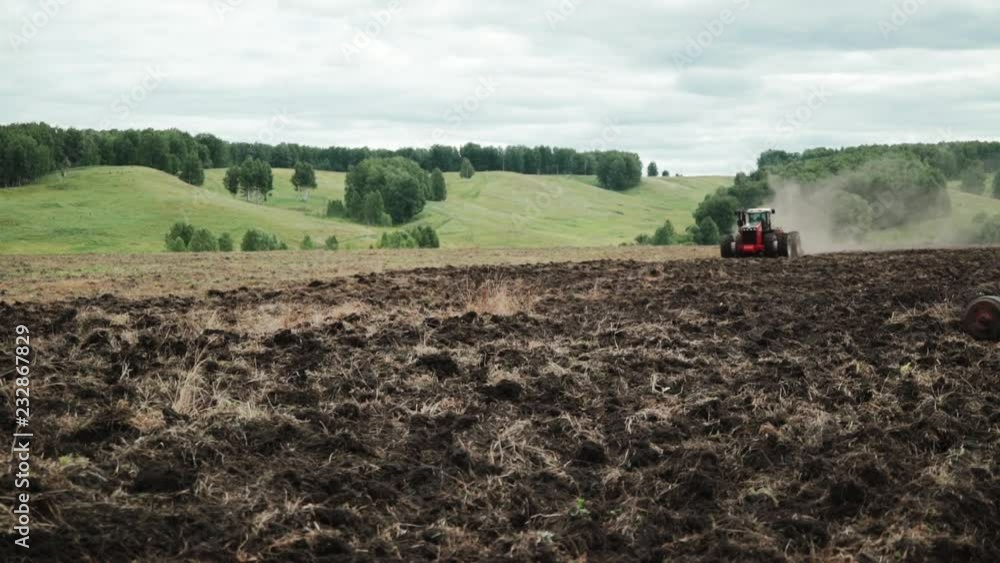 Red farm tractor plowing a field Red farm tractor plowing a field
