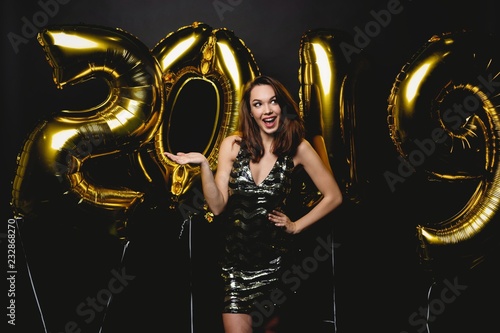 New Year. Woman With Balloons Celebrating At Party. Portrait Of Beautiful Smiling Girl In Shiny Dress Throwing Confetti, Having Fun With Gold 2019 Balloons On Background. High Resolution.