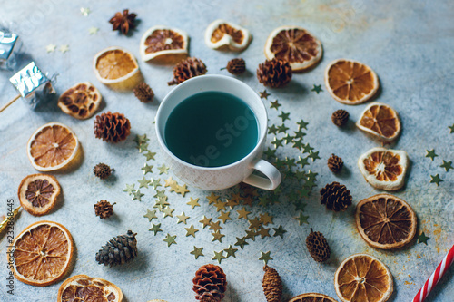 New Year or Christmas composition with blue tea, dry oranges, cones, cinnamon, candies and toys on light rustic table. Seasonal home decoration, winter holiday food, selective focus © Irina