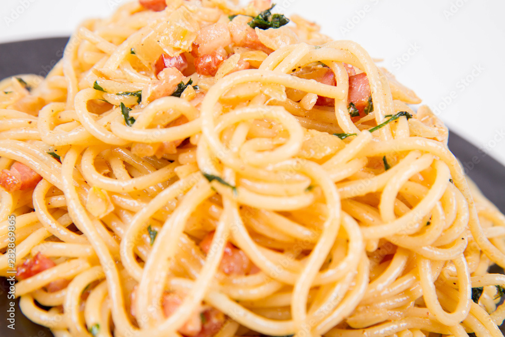 Spaghetti Carbonara with some parsley on a black plate on a white background Spaghetti Carbonara with some parsley on a black plate on a white background