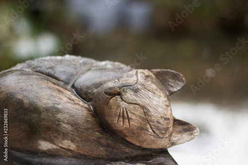 Close-up: image of a wooden cat sleeping on a windowsill is on a blurred natural background of falling sleet. Cold autumn day. Winter is coming.  © Olga