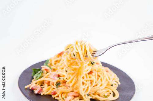 Spaghetti Carbonara with some parsley on a black plate on a white background being eaten with a fork