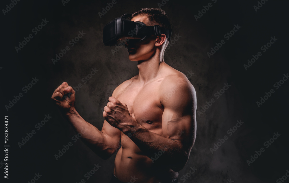 Young sportsman with muscular body wearing VR headset training punches in virtual reality fight on dark background.