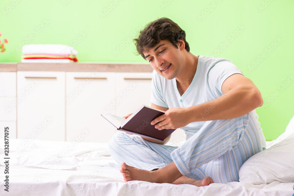 Fototapeta premium Young handsome student reading book in the bed 