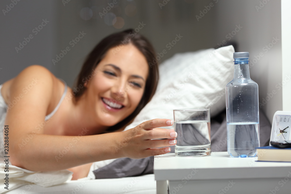 Happy girl catching a glass of water on the bed in the night Happy girl catching a glass of water on the bed in the night