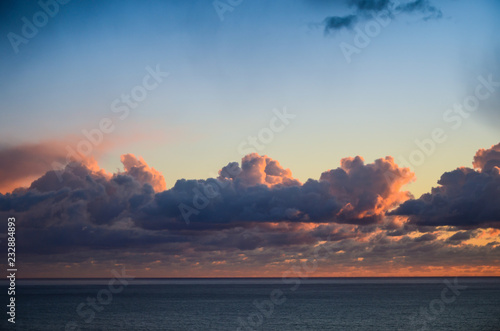Beautiful sunset glowing orange across the horizon under dramatic purple and pink clouds and bue sky over the Pacific Ocean along California's Big Sur coast