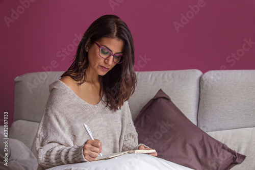 Tableau sur toile Mujer morena escribiendo a mano en el sofá en un cuaderno con bolígrafo y papel