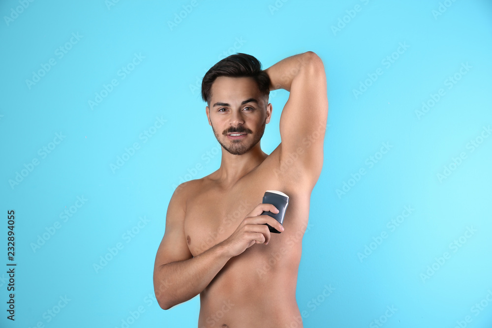 Young man using deodorant on color background