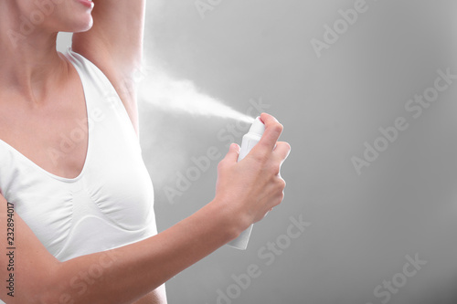 Young woman using deodorant on grey background, closeup. Space for text