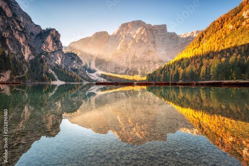 Beautiful Braies lake at sunrise in autumn in Dolomites, Italy. Landscape with mountains, gold sunlight, water with reflection, trees with orange leaves in fall. Travel in italian alps. Dolomiti photo