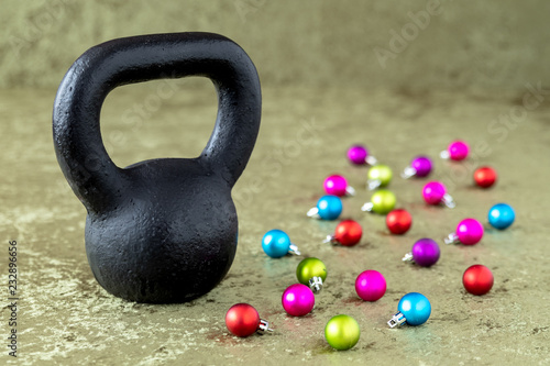 Black kettlebell on a green velvet background with colorful ball ornaments, holiday fitness