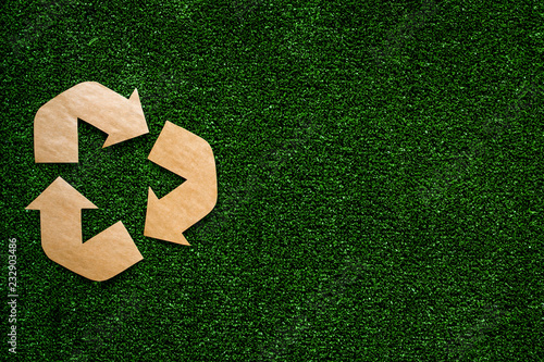 Eco recycle sign made of craft paper on green grass background top view copy space