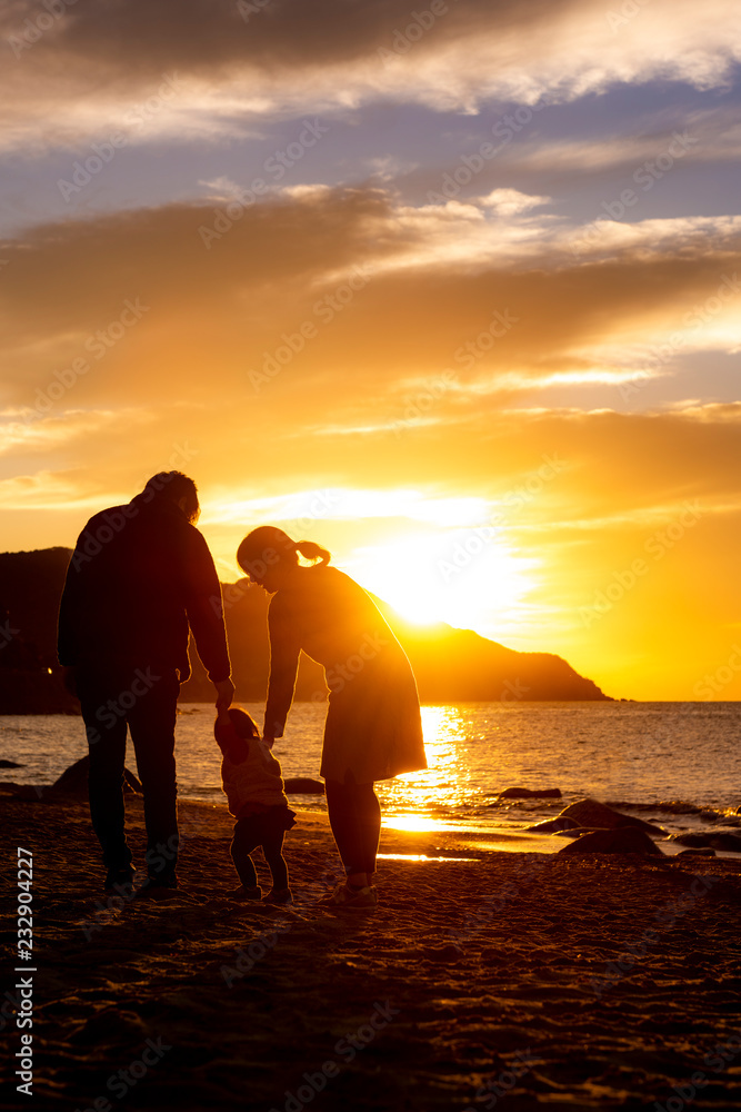 夕陽の沈む海岸と家族のシルエット