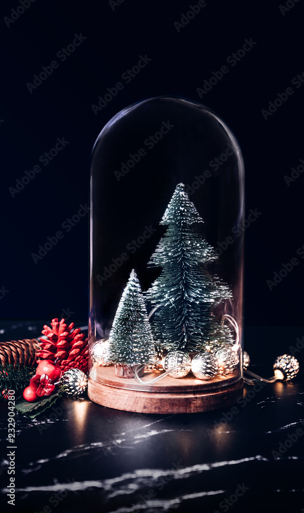 Merry Christmas with mistletoe and gift box icon with xmas tree and glowing light string and pine cone decoration on marble table and blue background.