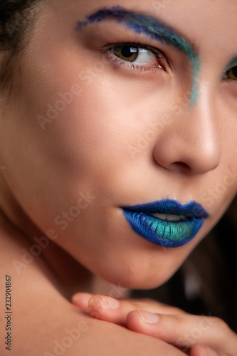 beautiful young Hispanic woman with a colorful top and blue lips has smooth skin and long flowing hair