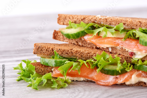 Sandwich with bread toasts, red fish salmon, fresh green leaves of salad and sliced cucumber