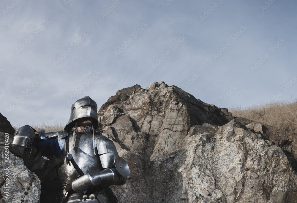Knight with a sword and in medieval armor on the background of granite stone Knight with a sword and in medieval armor on the background of granite stone